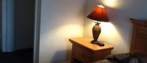 Et soveværelse med seng, natbord, lampe og et træskab.