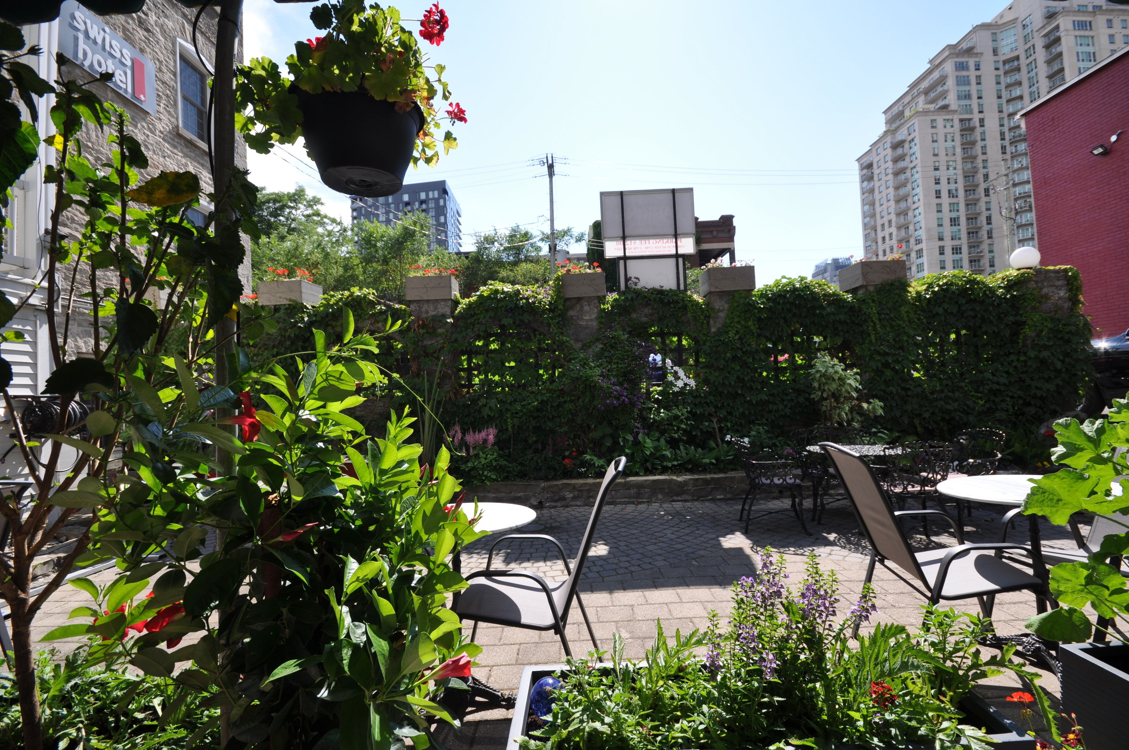 An outdoor patio area with tables and chairs, surrounded by greenery and a hanging flower pot.