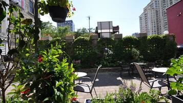 An outdoor patio area with tables and chairs, surrounded by greenery and a hanging flower pot.