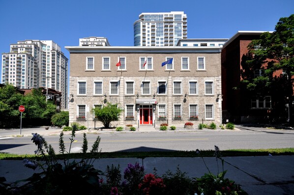 A two-story building with a red entrance, Swiss Hotel signage, and flags of the United States, Canada, and the European Union.