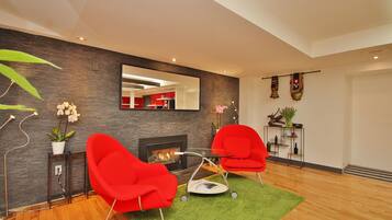 Una sala de estar moderna con dos sillones rojos, una mesita, una chimenea y un tapete verde.