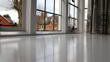 A room with a large window, a white floor, and a view of a brick house outside.