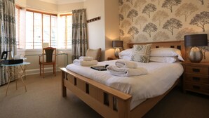 A neatly arranged bedroom with a large bed, a bedside table with lamps, a chair, and a small table with a kettle and cups. - B+B York (York)