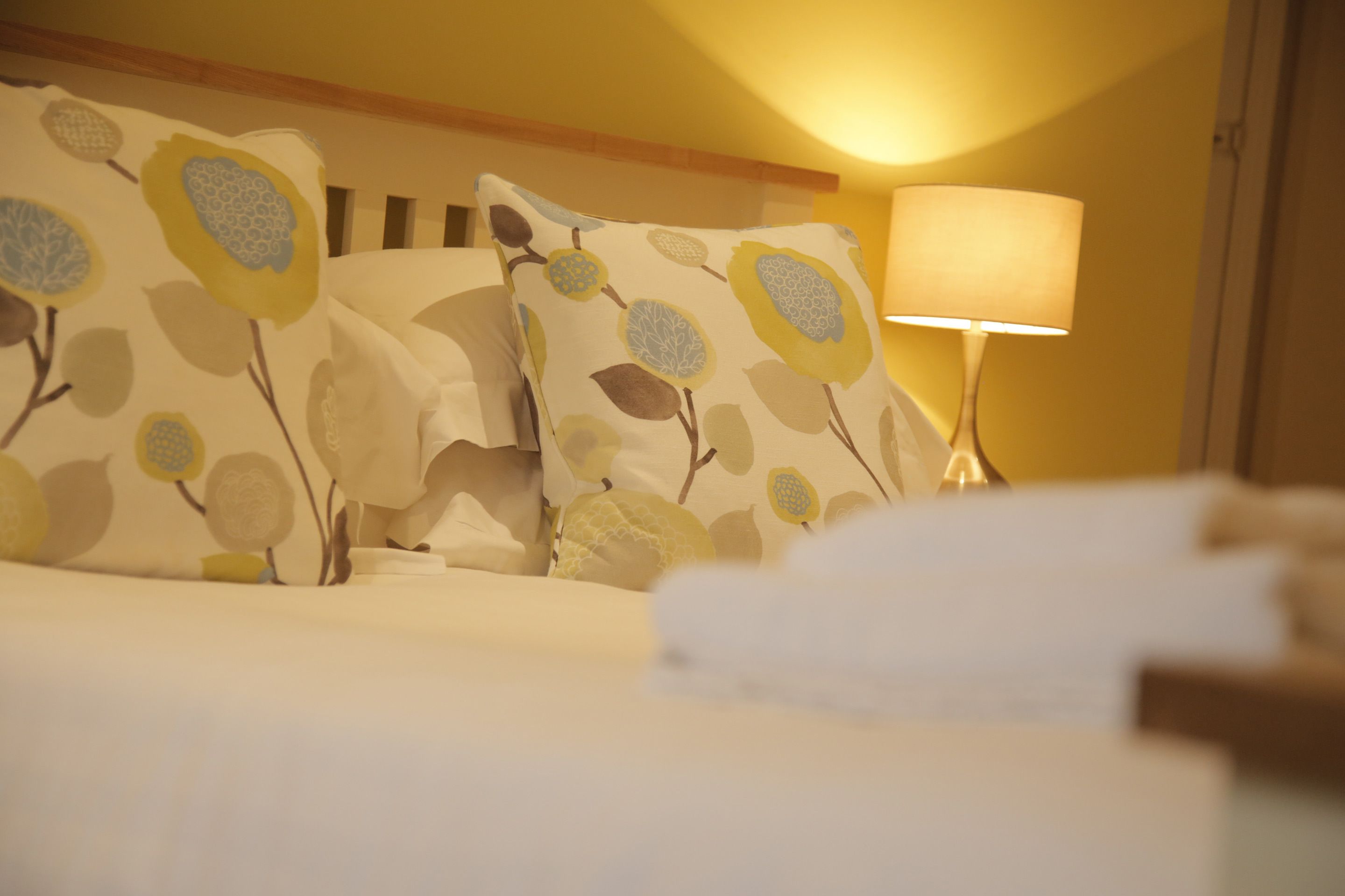 A hotel room with floral-patterned pillows, a bedside lamp, and neatly made beds.