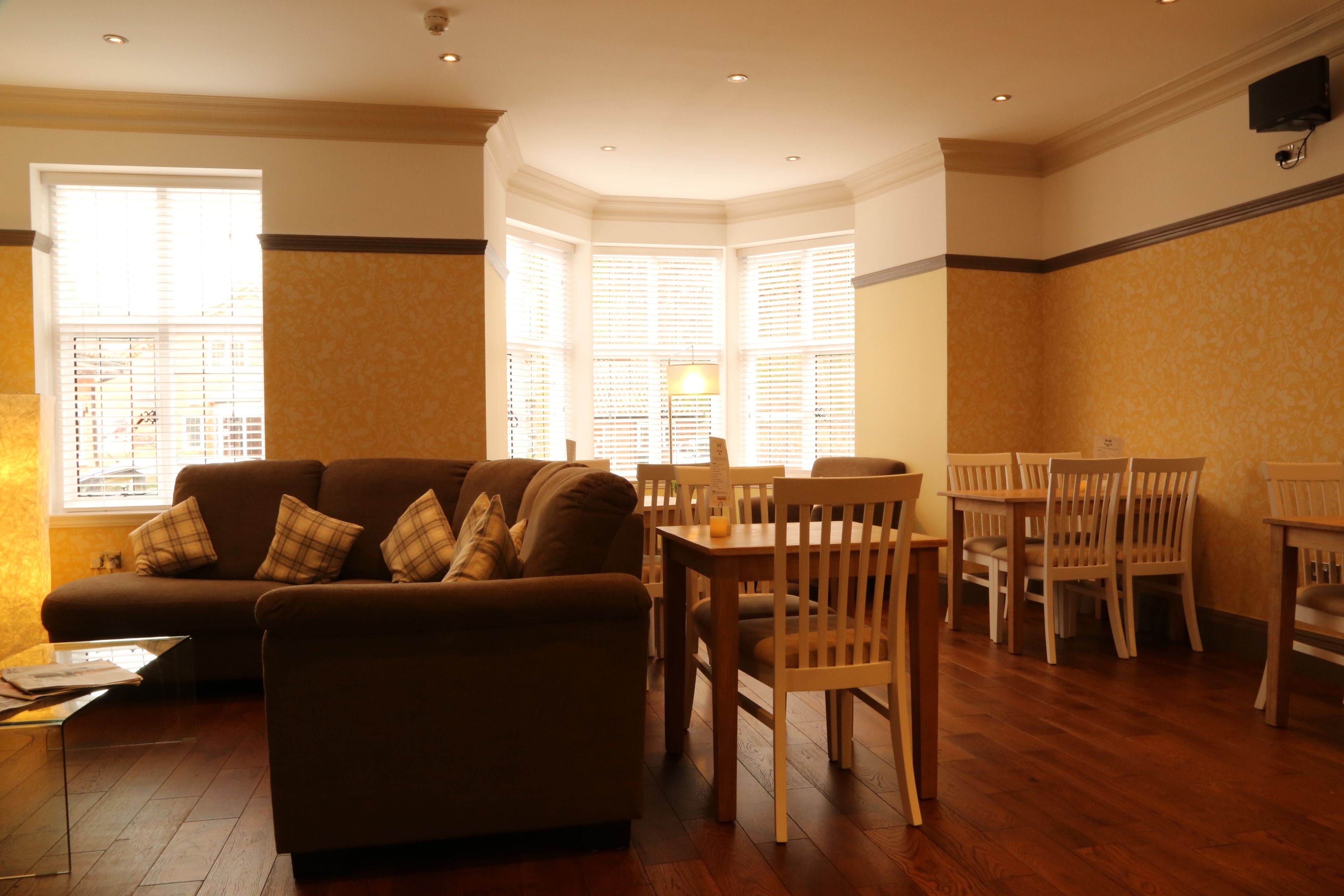 A living room with a sofa, wooden chairs, a glass coffee table, and a dining table.