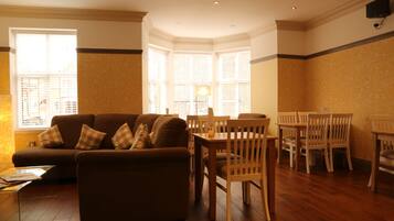 A living room with a sofa, wooden chairs, a glass coffee table, and a dining table.