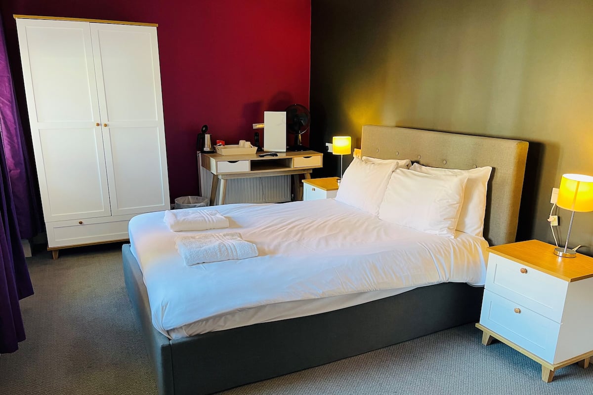 A hotel room with a bed, bedside tables, a desk, and a wardrobe.