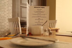 Un menú de desayuno sobre una mesa, junto a un tenedor, un cuchillo y saleros y pimenteros.