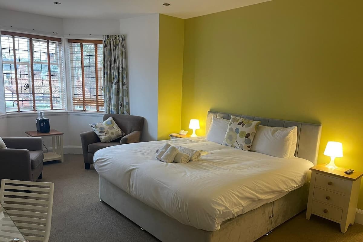 A hotel room with a large bed, two bedside tables with lamps, a chair, and a small table with a lamp.