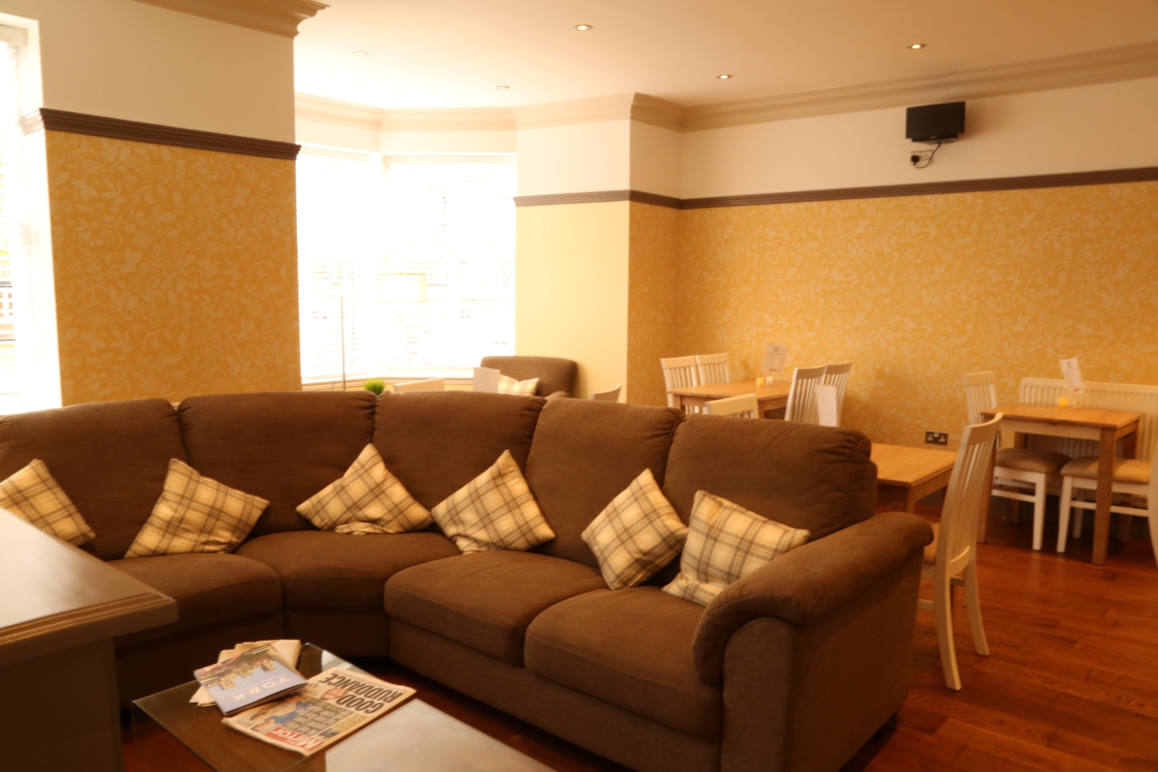 A living room with a brown sectional sofa, a coffee table with magazines, and a dining area with a table and chairs.