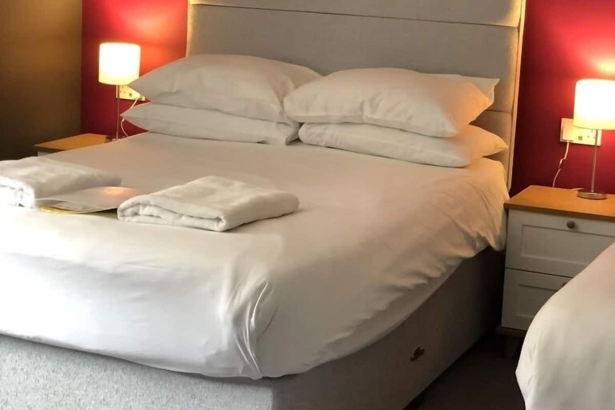 A neatly made bed with white linens and pillows, a headboard, and bedside tables with lamps.