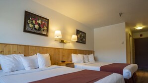 A hotel room with two beds, wooden headboard, white bedding, and two wall-mounted lamps.