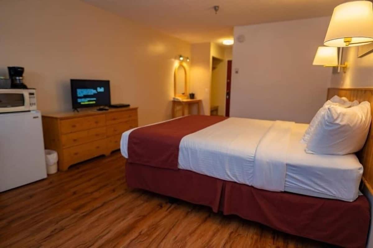 A hotel room with a bed, a television, a microwave, a dresser, and a lamp.