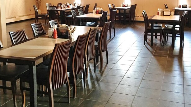 A restaurant with multiple tables and chairs, a tiled floor, and a wooden ceiling.
