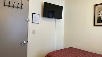A room with a bed, a door with a coat rack, a mounted television, and a framed picture on the wall.