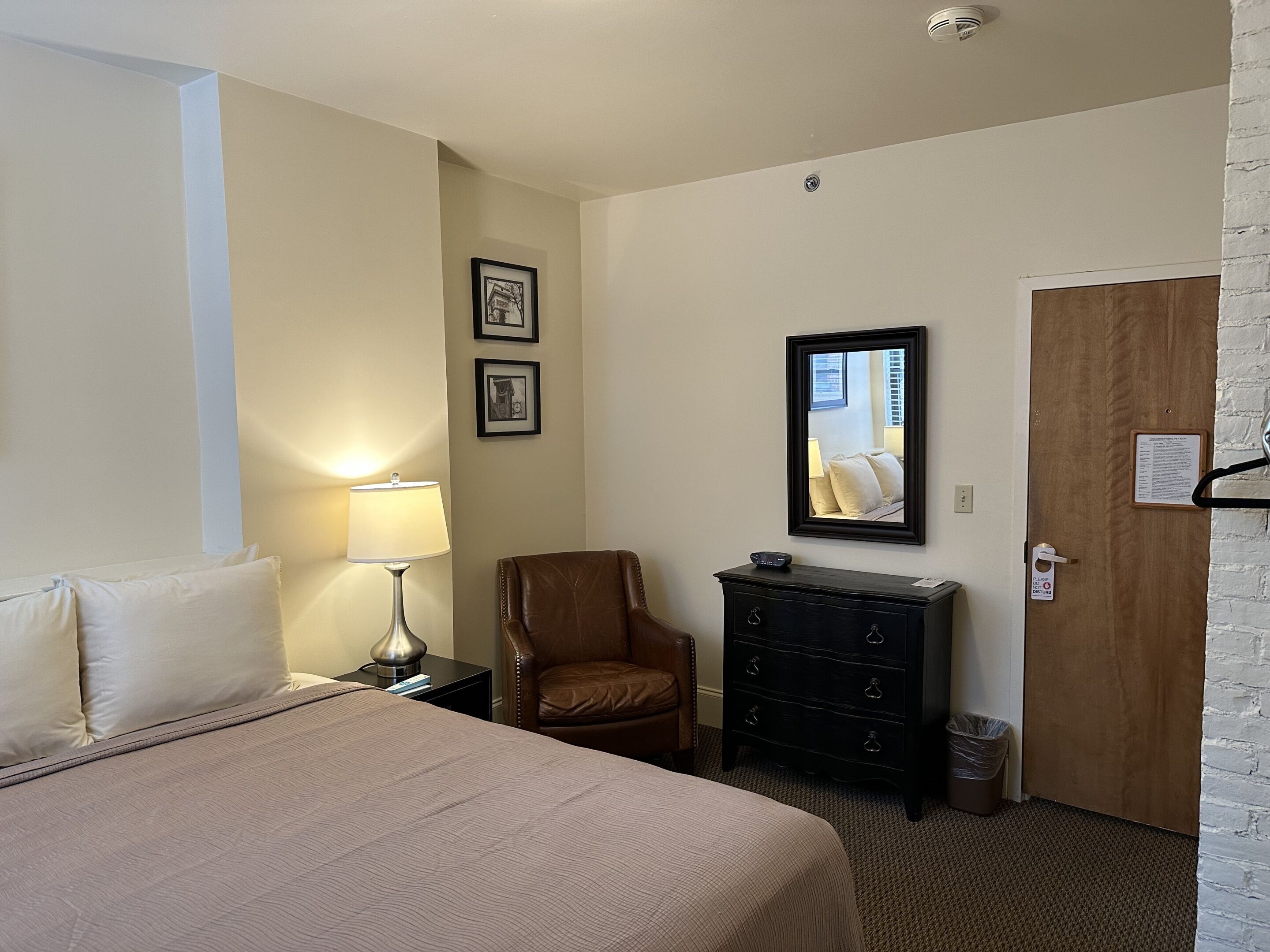 Una habitación de hotel con una cama, una silla, un aparador y una puerta.