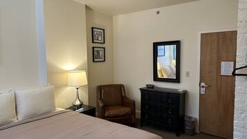 Una habitación de hotel con una cama, una silla, un aparador y una puerta.