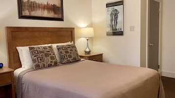 A neatly made bed with patterned pillows, a wooden headboard, a bedside table with a lamp, and a framed artwork above the bed.