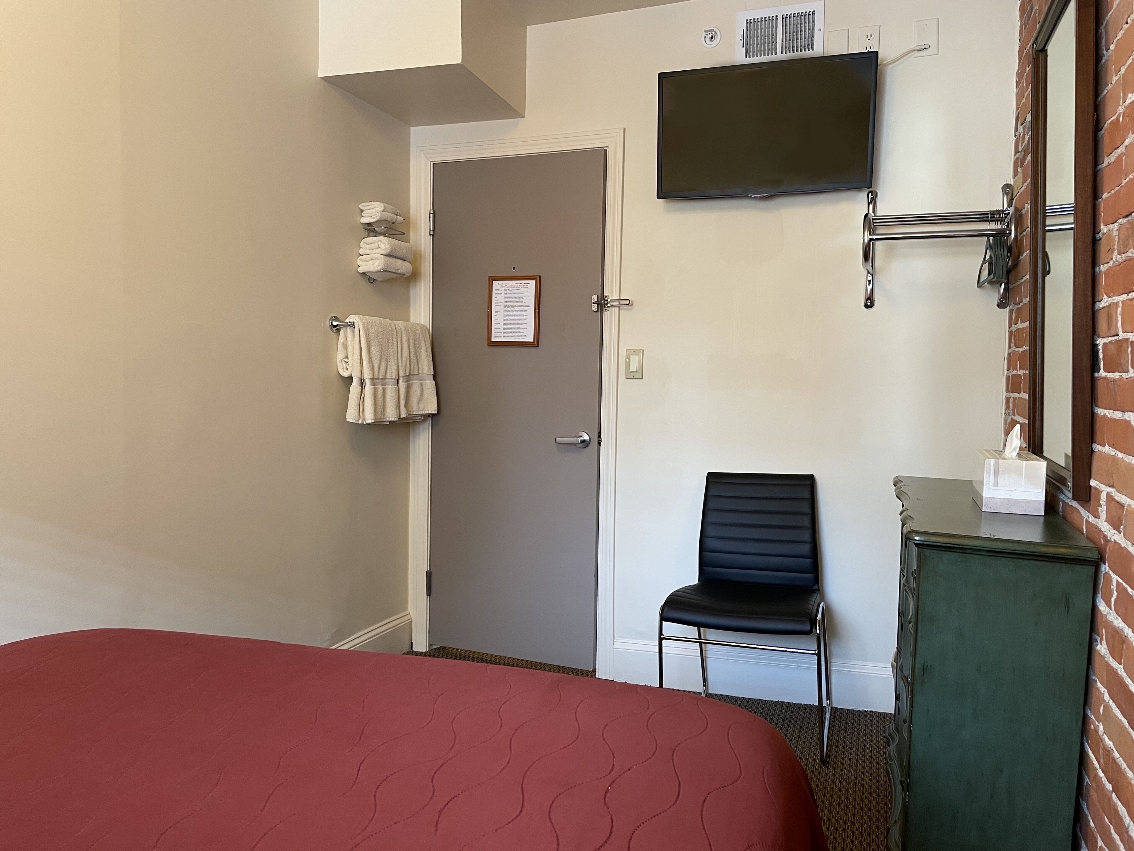 Una camera d'albergo con un letto, una sedia, una televisione a parete e un portasciugamani.