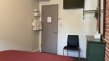 Una camera d'albergo con un letto, una sedia, una televisione a parete e un portasciugamani.