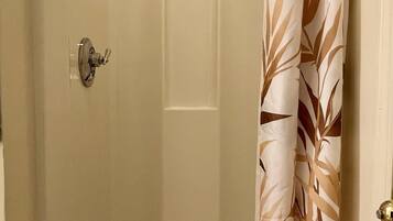 Une douche à l’italienne avec un pommeau de douche, un drain et un rideau orné d’un motif de feuilles.