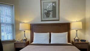 Ein Hotelzimmer mit einem großen Bett, zwei Nachttischen mit Lampen, einem Telefon und einem gerahmten Bild an der Wand.