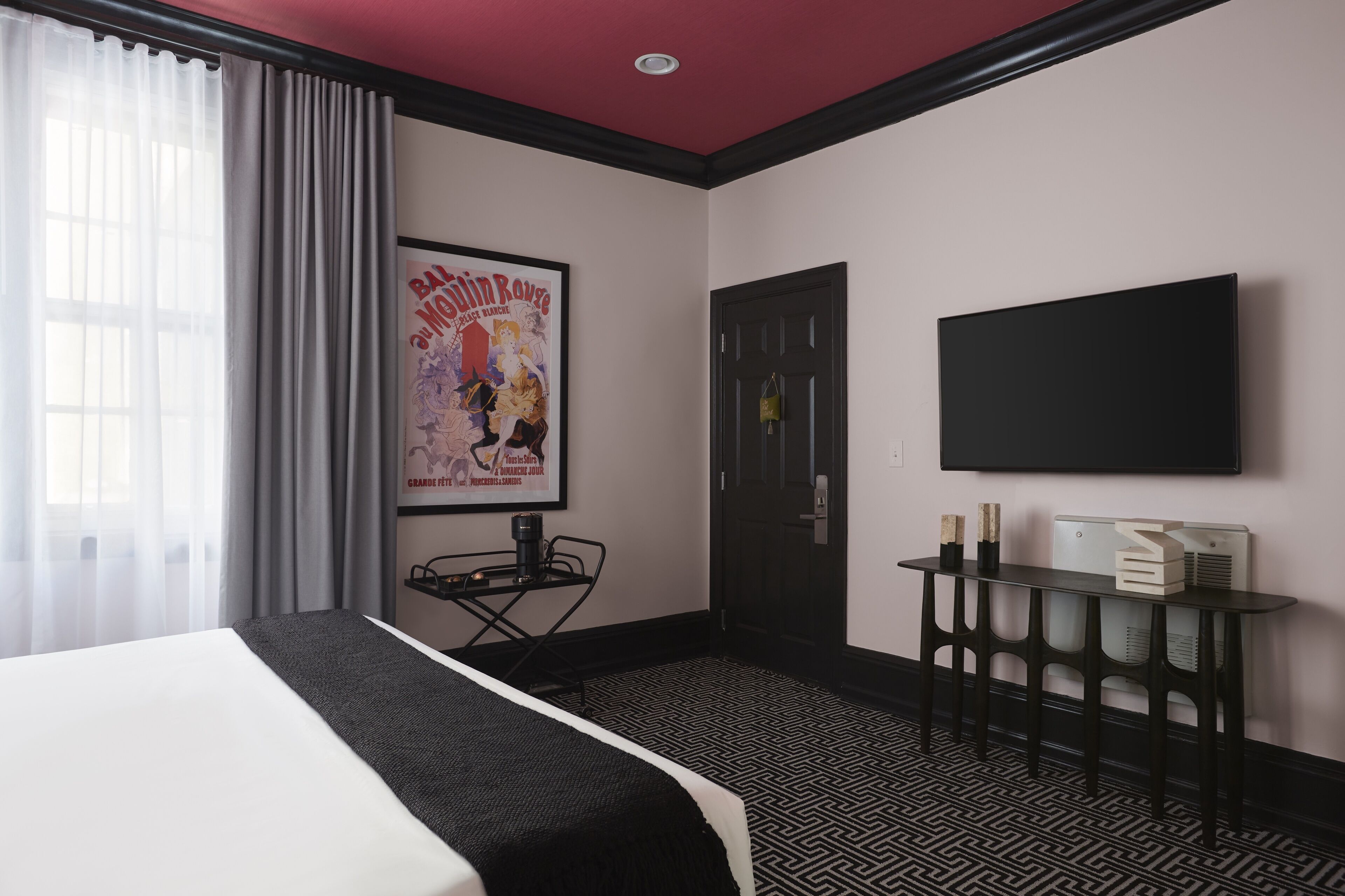 A hotel room with a bed, a desk with a chair, a television, and a poster on the wall.