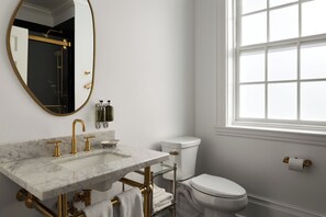 A bathroom with a marble sink, gold fixtures, a toilet, and a window with white panes.