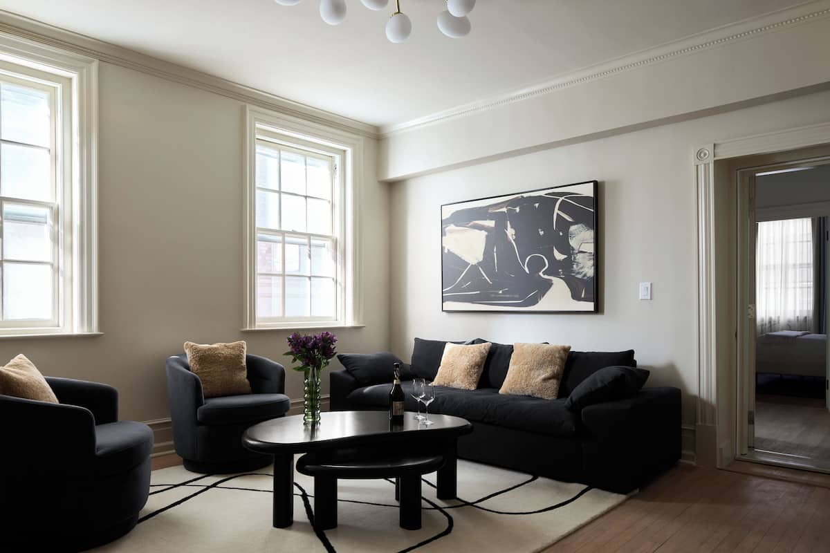 A modern living room with a black sofa, two armchairs, a coffee table, and a large abstract painting on the wall.