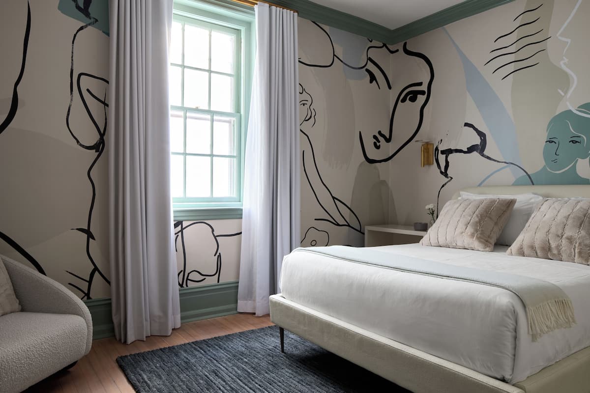 A bedroom with a large bed, a nightstand, a lamp, and a window with curtains.