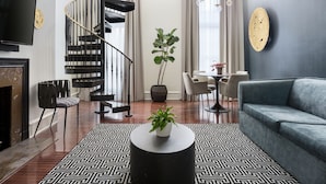 A modern living room with a black spiral staircase, a grey sofa, a round coffee table with a plant, and a patterned rug. - The Franklin on Rittenhouse, A Boutique Hotel (Philadelphia)