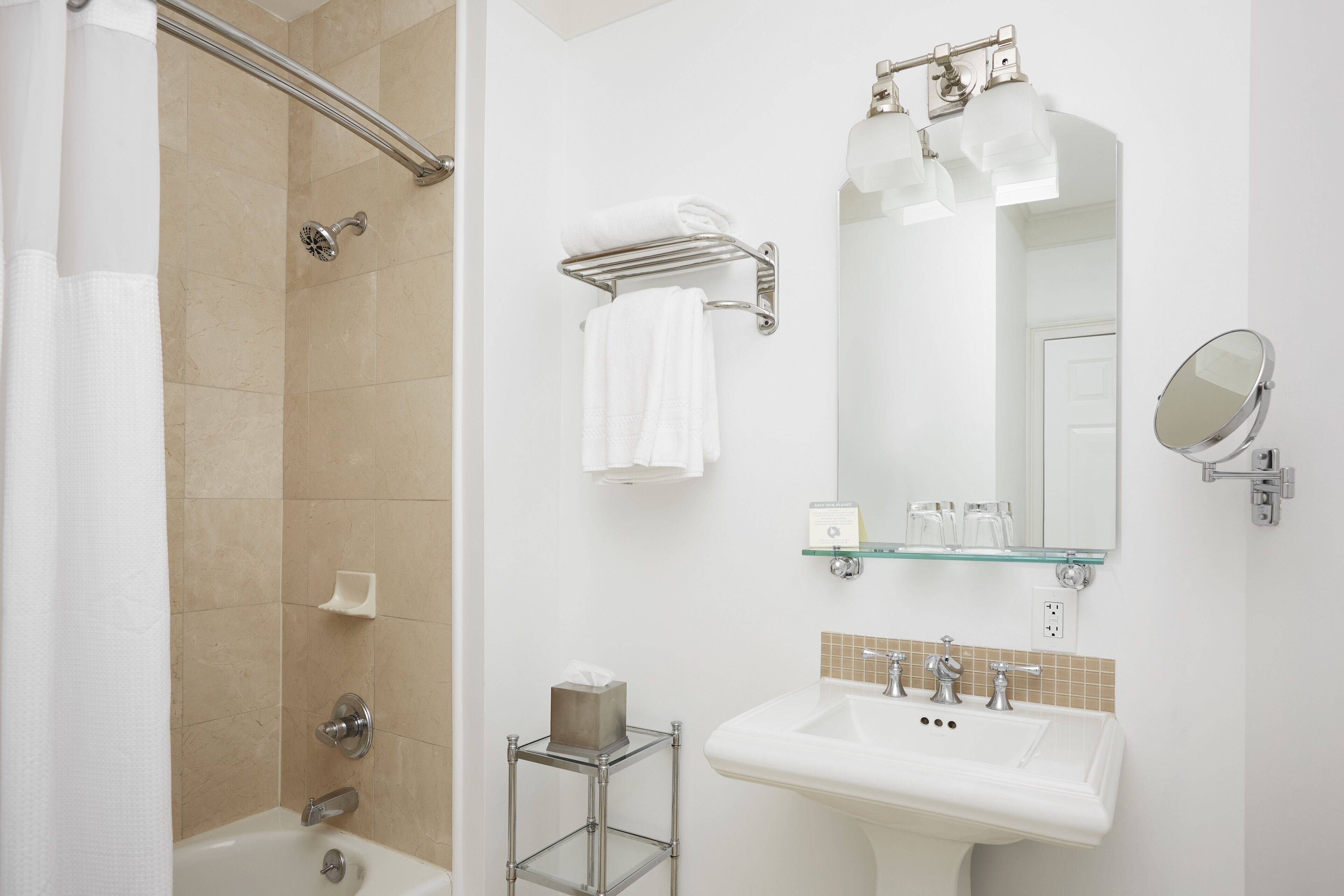 Een badkamer met een douche, een wastafel, een glazen plank met toiletartikelen en een spiegel.