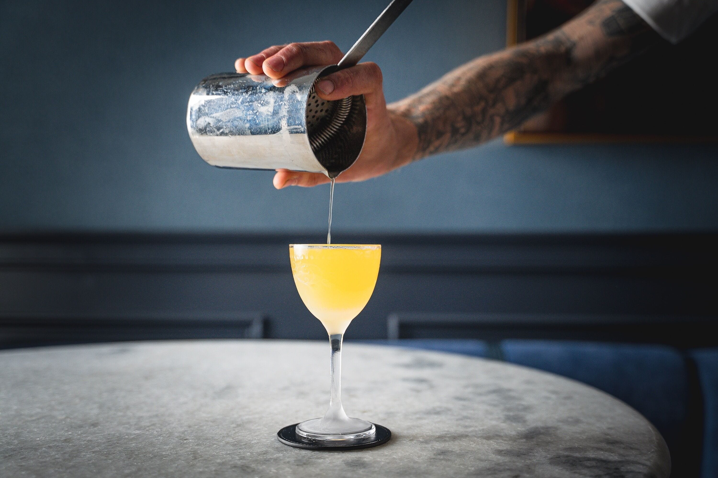 A person pouring a drink into a martini glass on a round table.