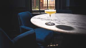 A round table with a single glass of a yellow beverage, two blue chairs, and a window with a view of a brick building. - The Franklin on Rittenhouse, A Boutique Hotel (Philadelphia)