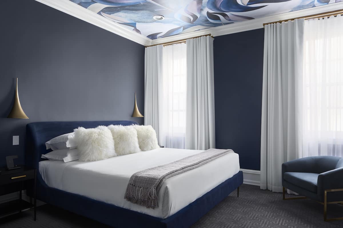 A modern bedroom with a large bed, two bedside tables, a chair, and a ceiling with a unique design.