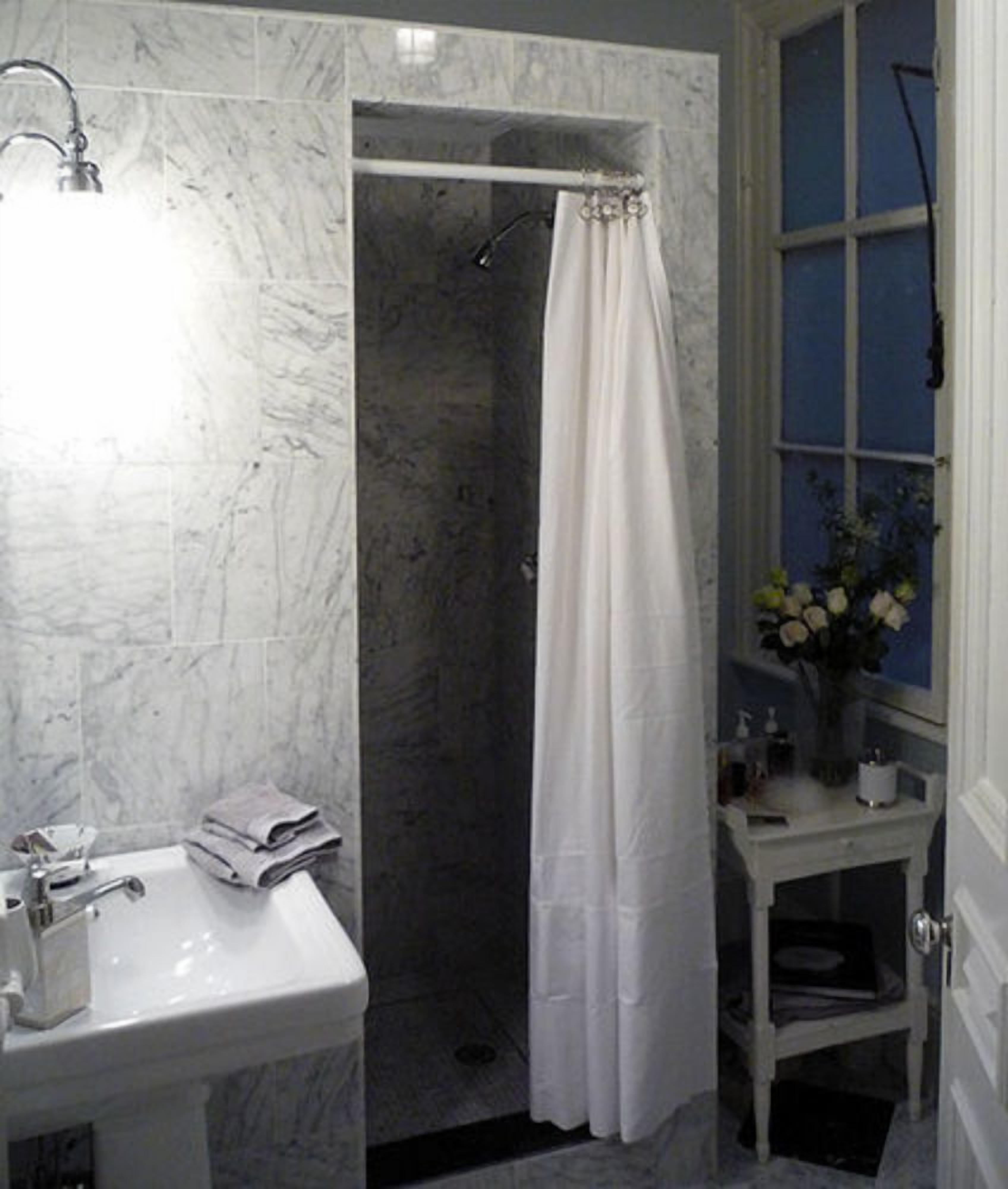 A bathroom with a white sink, a shower with a white curtain, and a window with a blue frame.