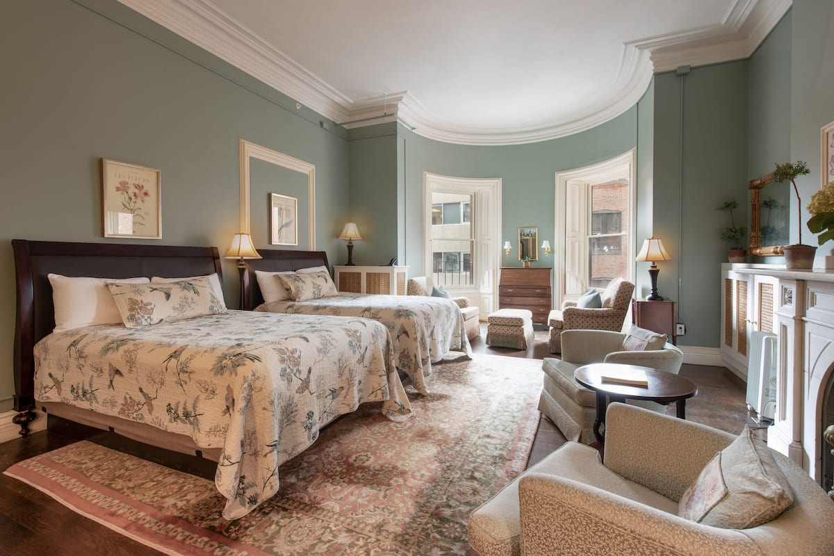 A spacious bedroom with a large bed, two smaller beds, a sitting area with a sofa and armchairs, and a fireplace.