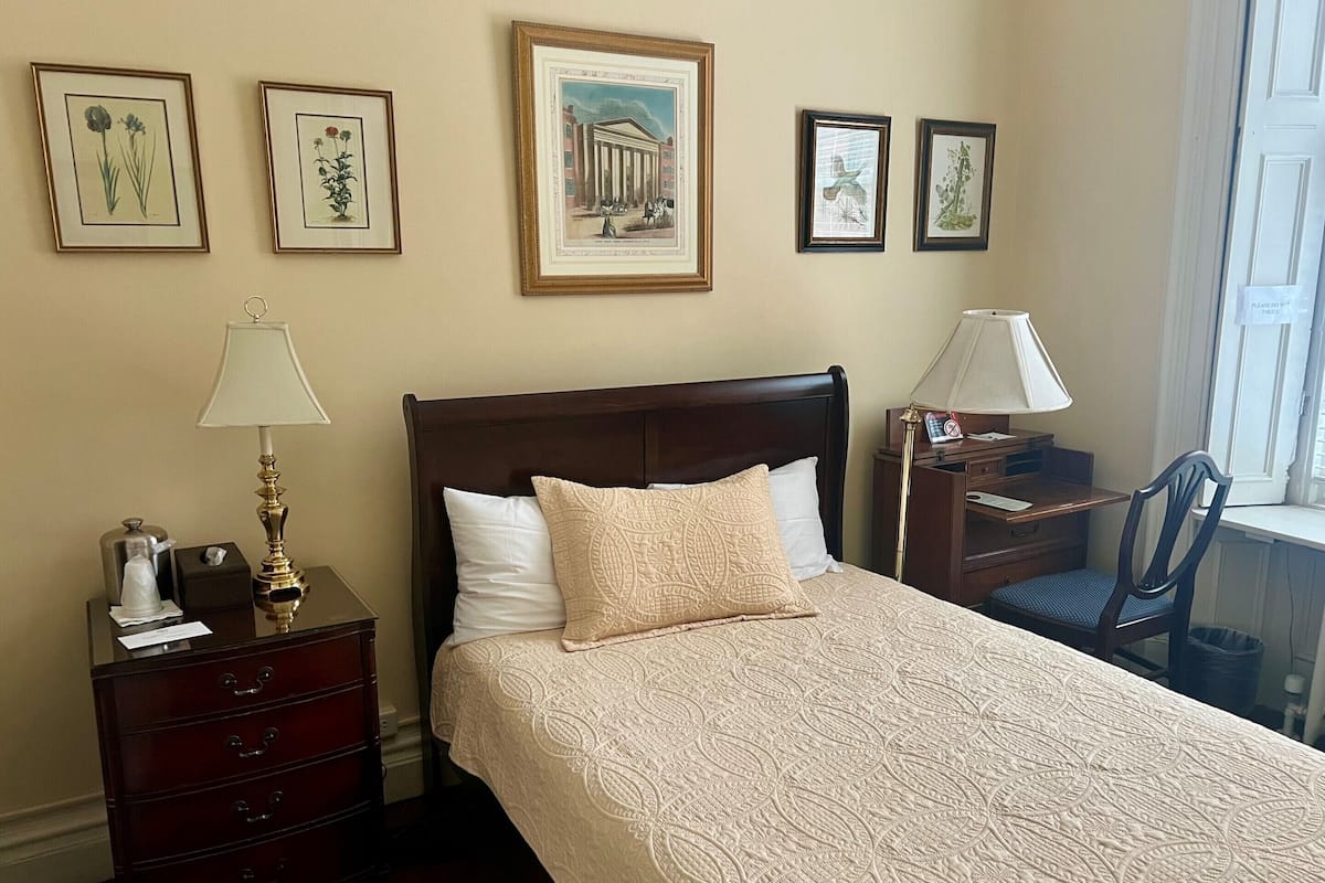 A hotel room with a bed, a nightstand, a lamp, a chair, and framed pictures on the wall.