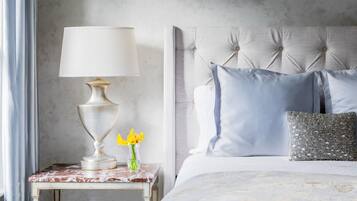 Een net opgemaakt bed met een gestoffeerd hoofdbord, een nachtkastje met een lamp, en een vaas met gele bloemen.