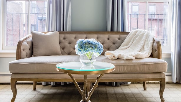 A beige sofa with a glass coffee table in front, a white throw blanket, and a vase of blue flowers. - Clarendon Square (Boston)
