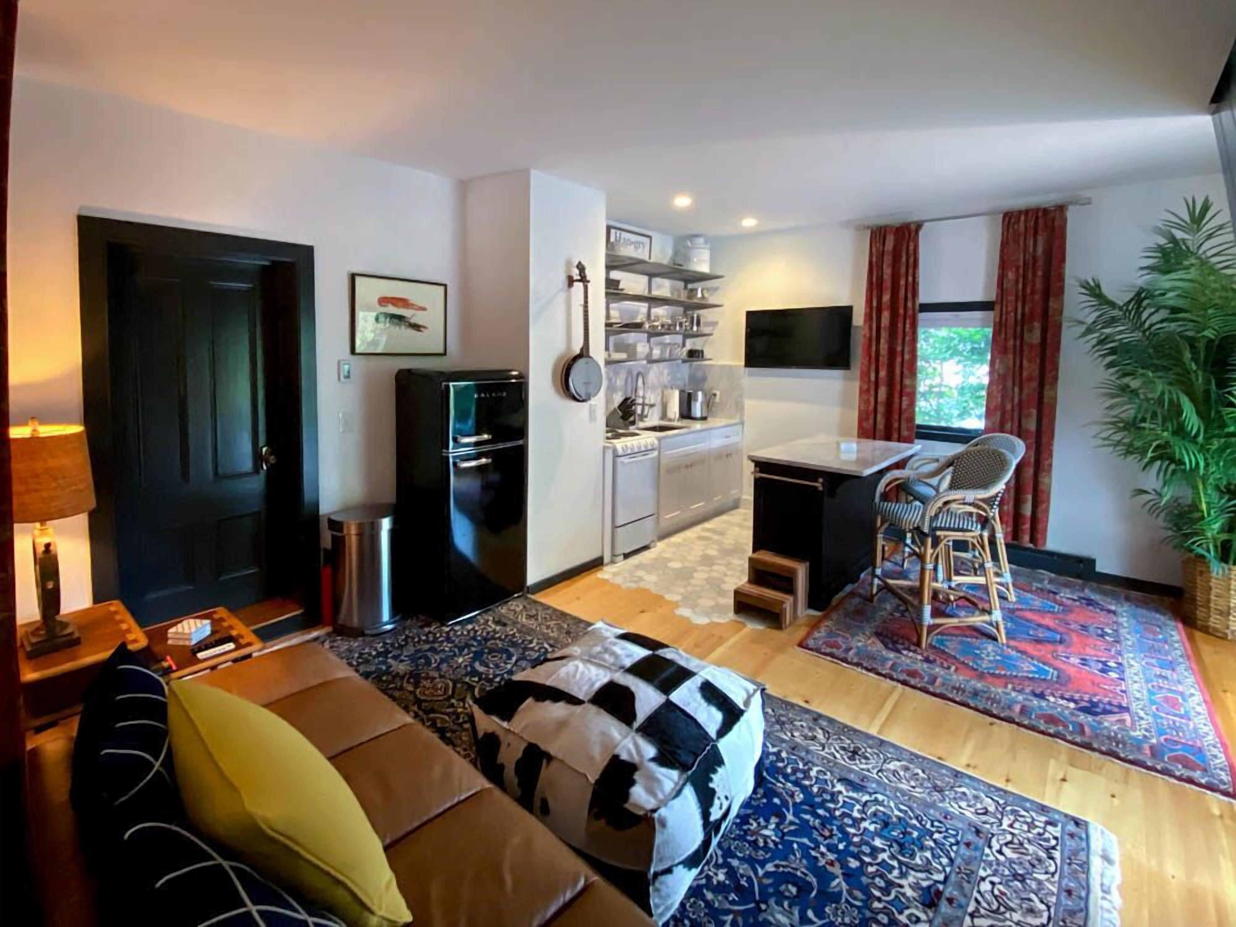 Un espacio habitable compacto con kitchenette, zona de comedor y sofá con cojines.