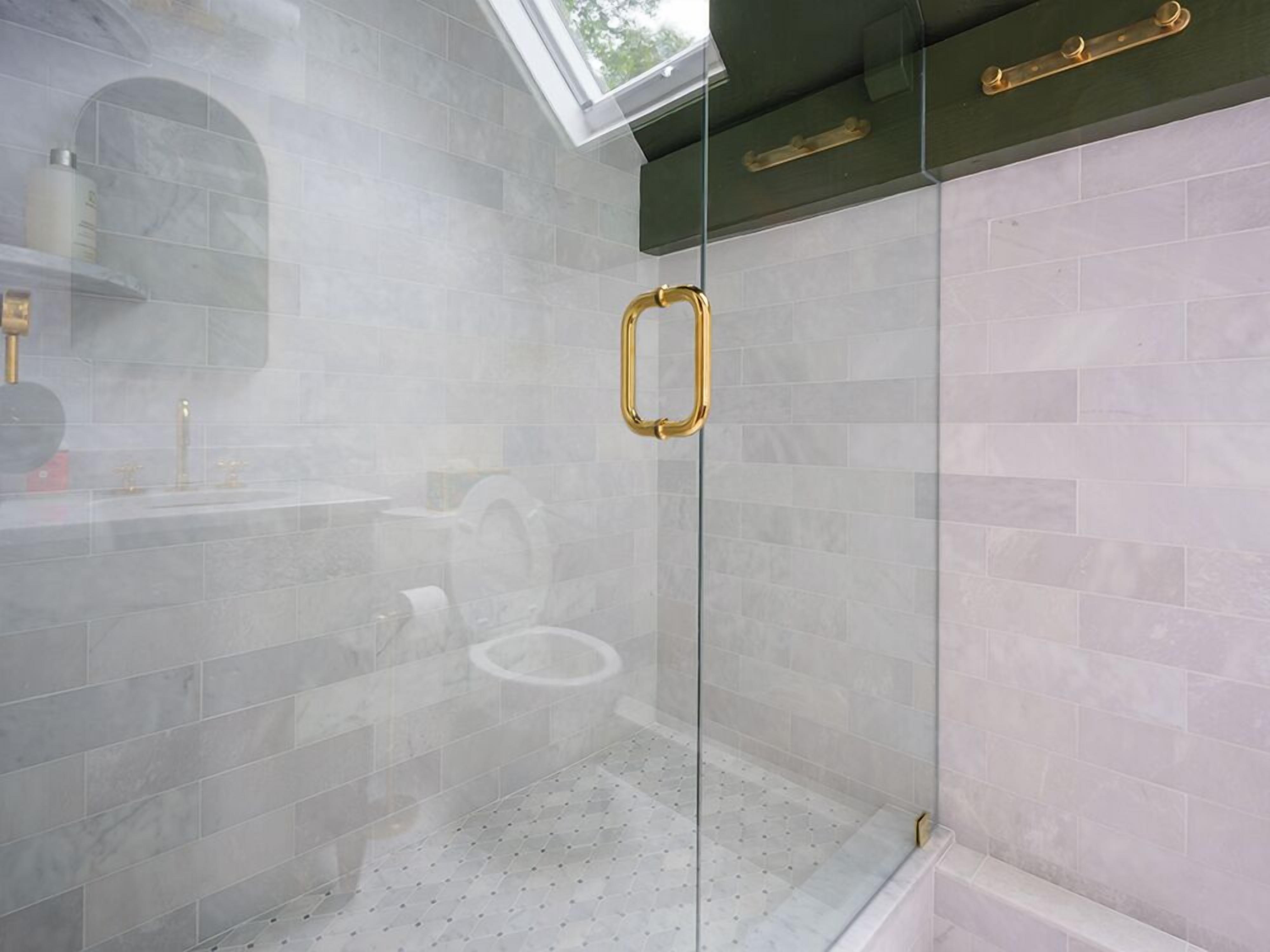 Een moderne badkamer met een douchecabine van glas, een dakraam en een wand betegeld met marmer.