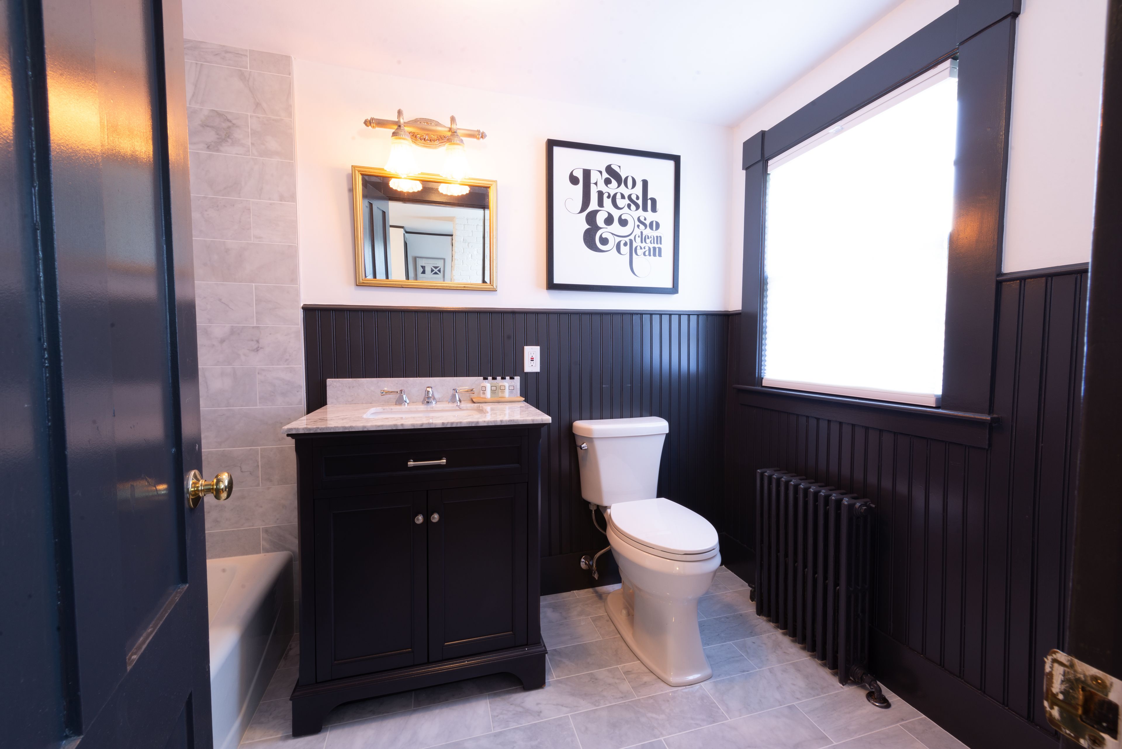 A bathroom with a dark wood vanity, a white toilet, and a large window.