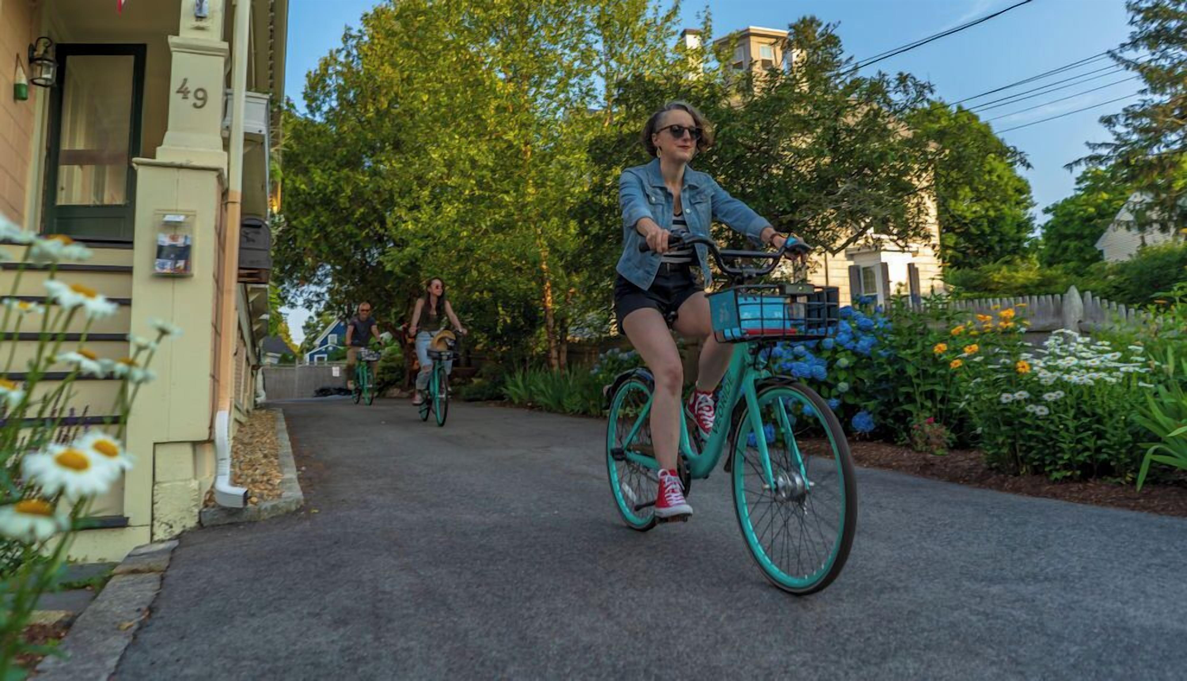 A residential street with houses, a paved path, and cyclists.
