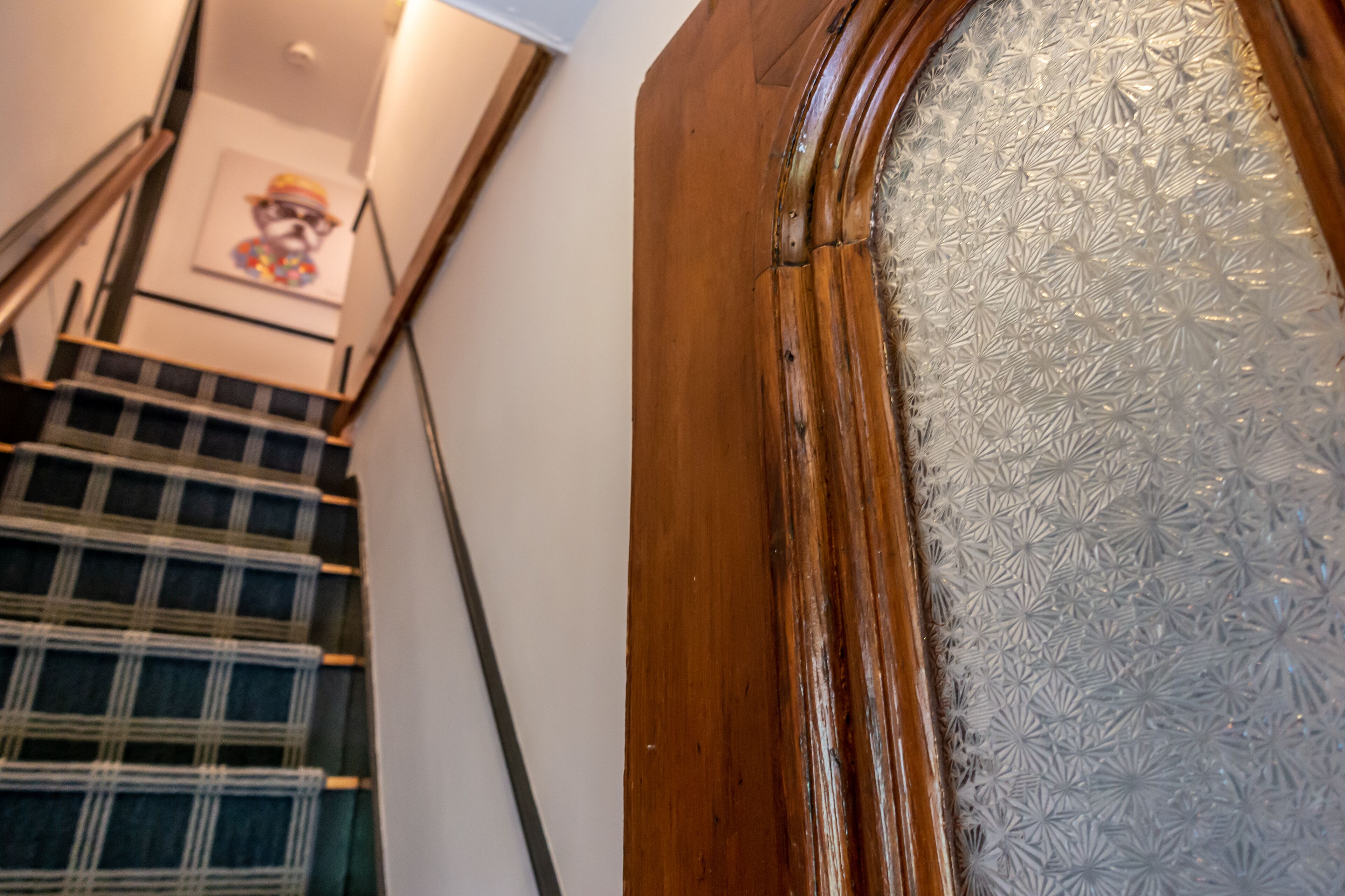 A staircase with a checkered pattern, a wooden door with frosted glass, and a framed picture on the wall.