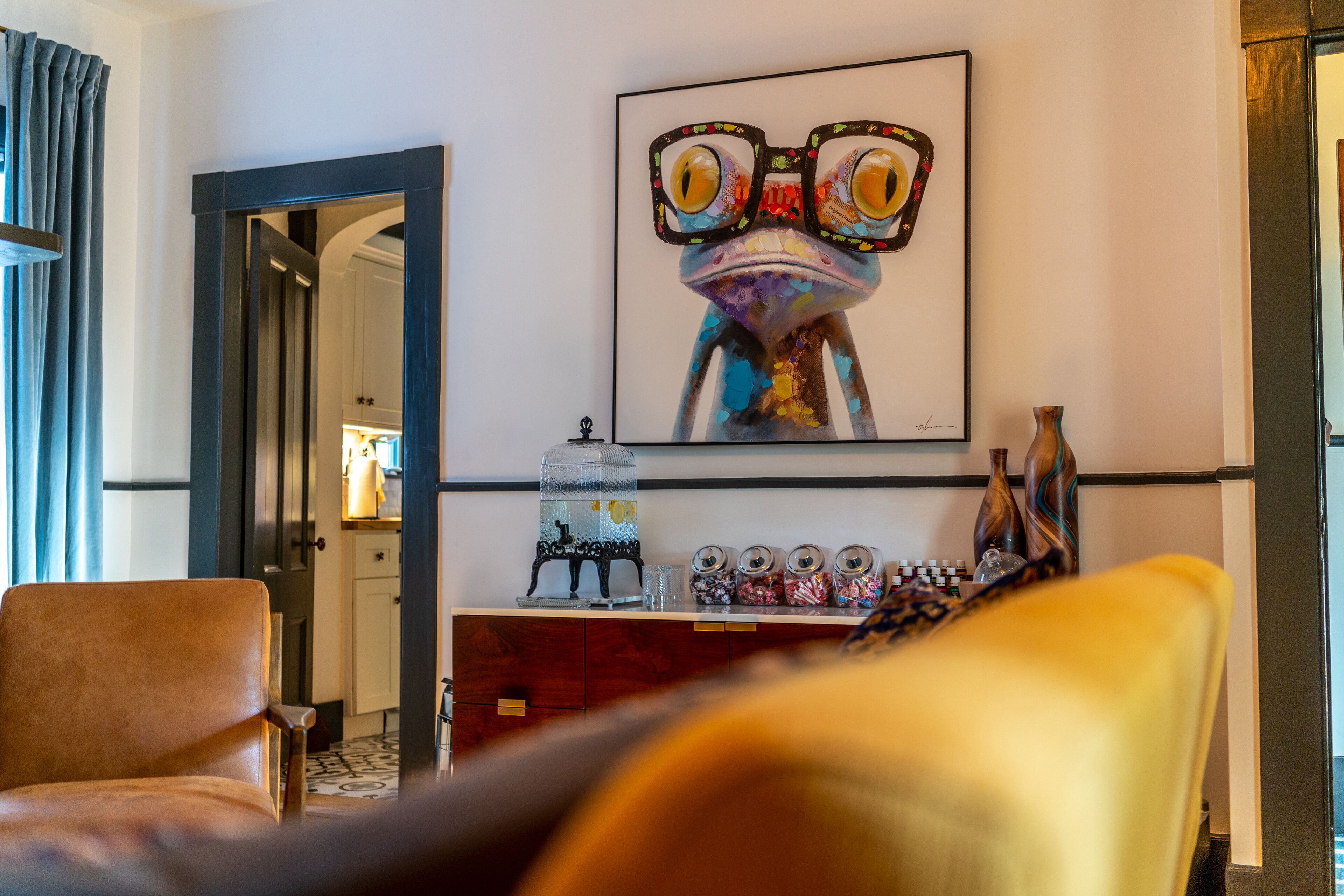 Ein Hotelzimmer mit einem großen Froschgemälde, einer Holzkabine mit Dekorationsobjekten und einem gelben Stuhl.