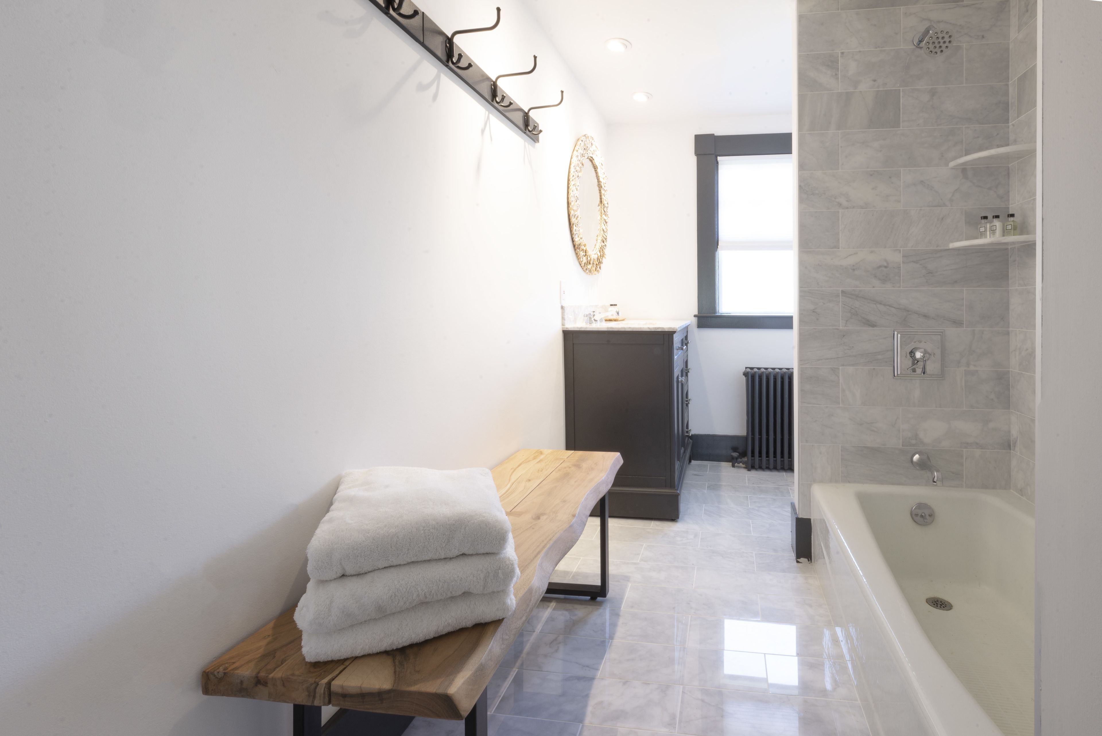 A modern bathroom with a wooden bench, a bathtub, and a shower area.