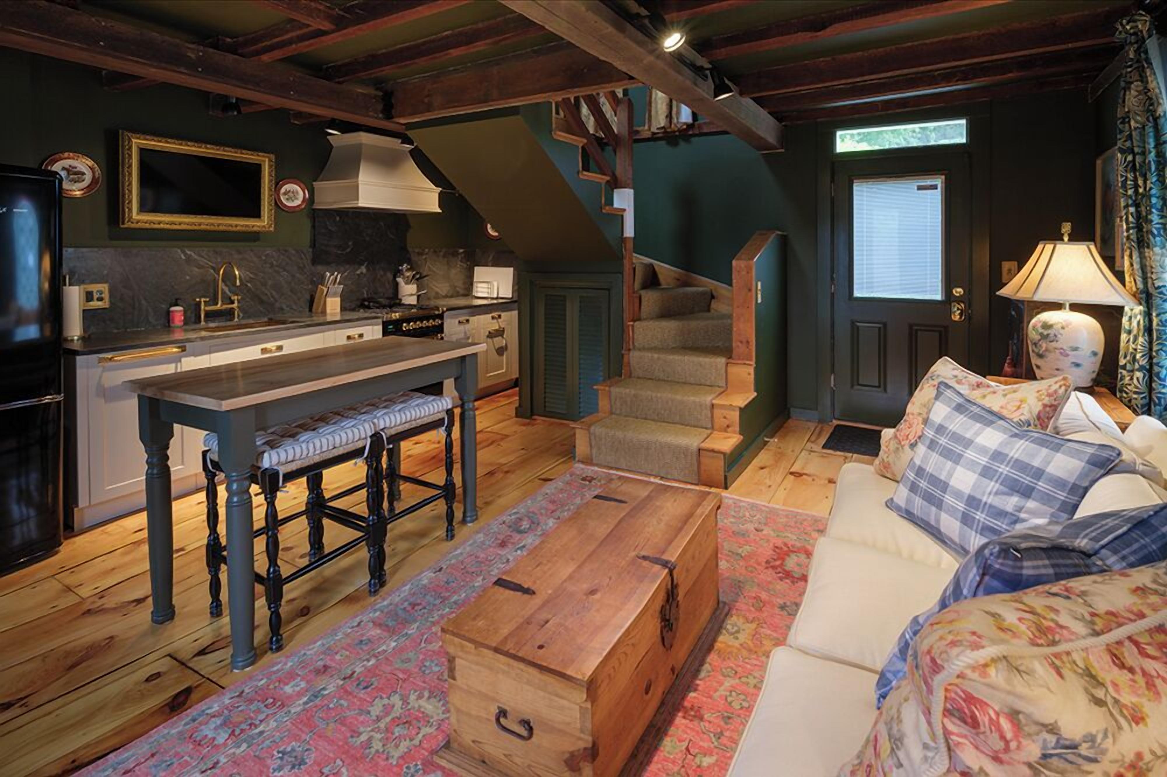 Uma sala de estar acolhedora com um sofá, um baú de madeira e uma escada que leva a um quarto escuro.