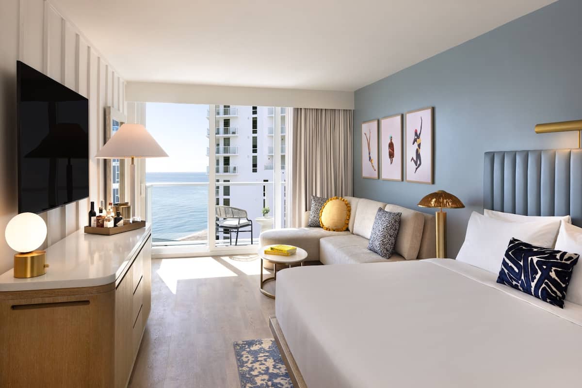 Habitación de hotel con cama, sofá, televisión, escritorio y vista al océano.