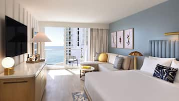 A hotel room with a bed, a desk, a chair, a sofa, a TV, and a view of the ocean.